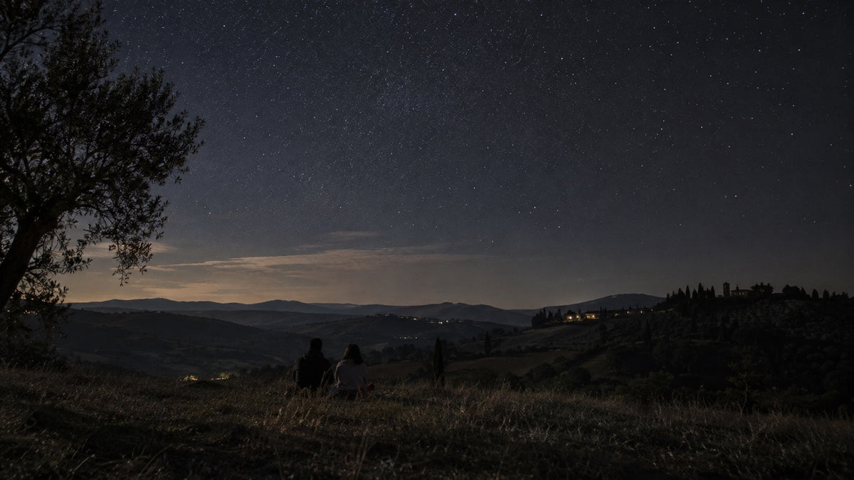 Due persone osservano un cielo stellato da una collina italiana